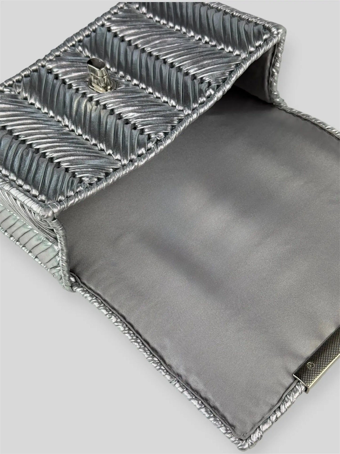 Brilliant Silver is a luxury handmade mini designer bag by CATTLEYA.Y, defined by its luminous metallic finish and refined chevron texture. The cool silver tone reflects light effortlessly, creating a striking yet sophisticated presence.
Grey satin lining inside Brilliant Silver luxury bag