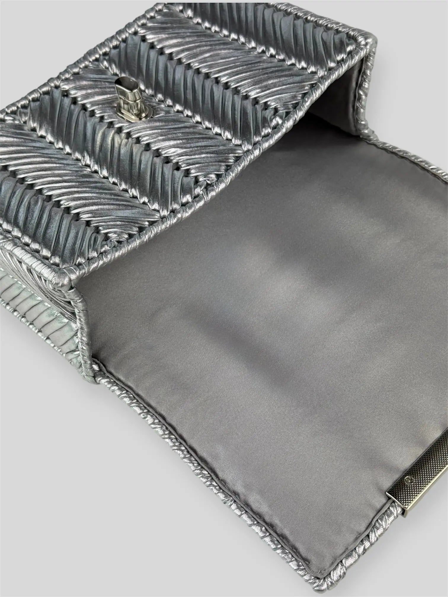 Brilliant Silver is a luxury handmade mini designer bag by CATTLEYA.Y, defined by its luminous metallic finish and refined chevron texture. The cool silver tone reflects light effortlessly, creating a striking yet sophisticated presence.
Grey satin lining inside Brilliant Silver luxury bag